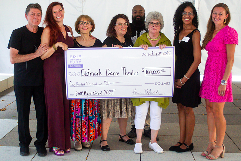 A group of eight people smiles while holding a large check for $100,000 made out to Dafmark Dance Theater from the Erie Womens Fund. The check is dated July 29, 2025.